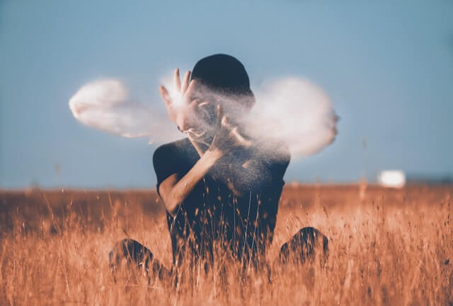 man sitting in a brown grass field playing with smoke